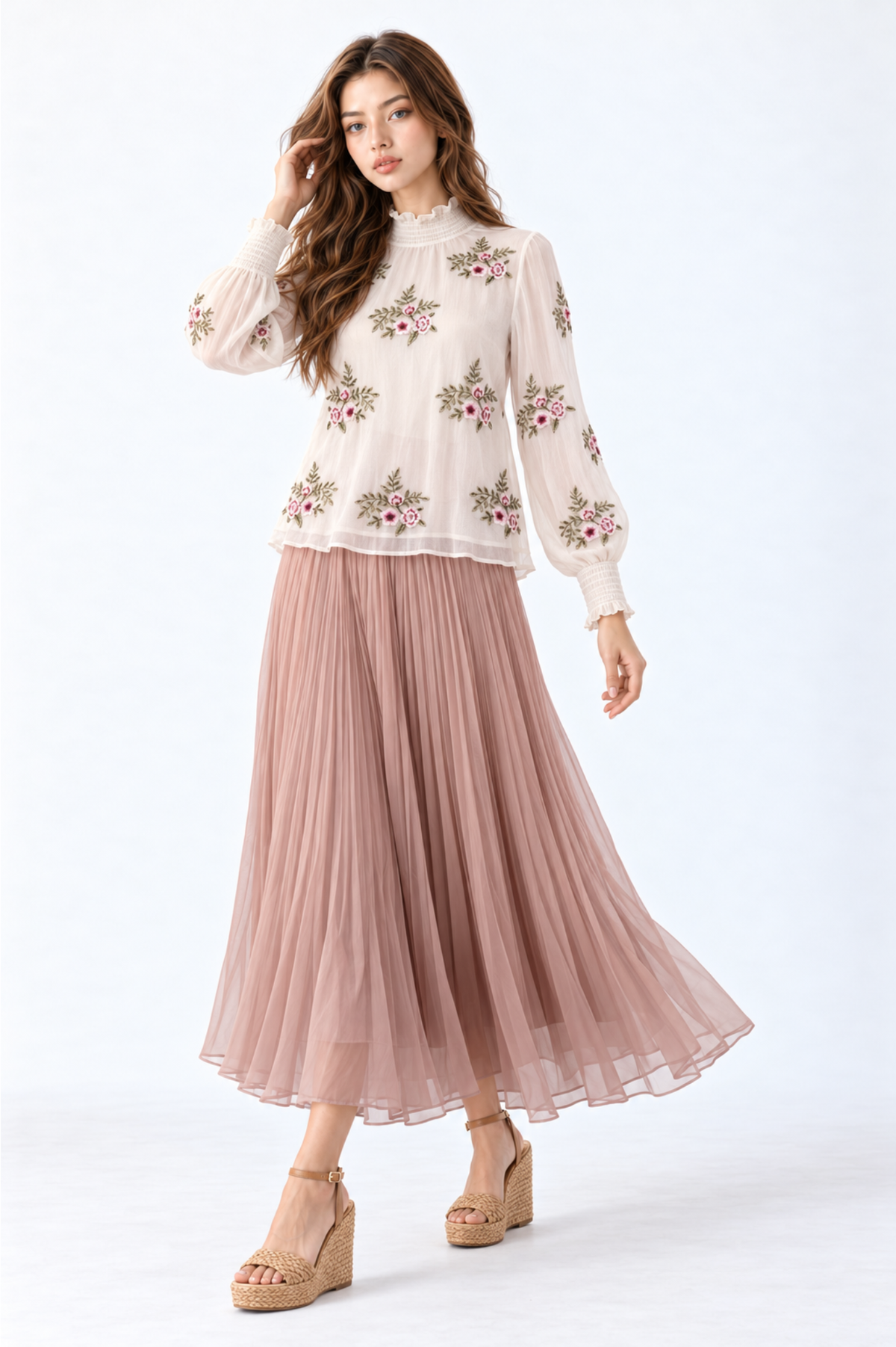 Model wearing an ivory floral embroidered blouse with high ruffled neckline, long puff sleeves and smocked cuffs, styled with a dusty pink pleated maxi skirt and wedge sandals.