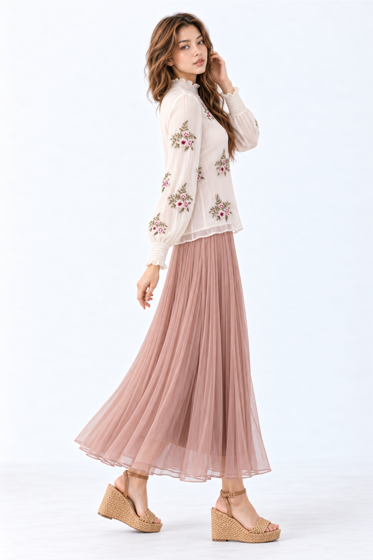Model wearing an ivory floral embroidered blouse with high ruffled neckline, long puff sleeves and smocked cuffs, styled with a dusty pink pleated maxi skirt and wedge sandals.