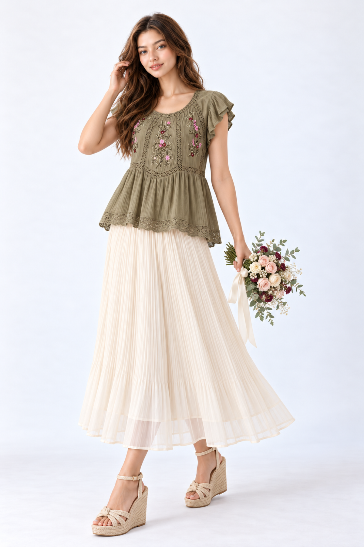 Model wearing an olive green floral embroidered peplum blouse with flutter sleeves and round neckline, styled with a cream pleated maxi skirt and wedge sandals.