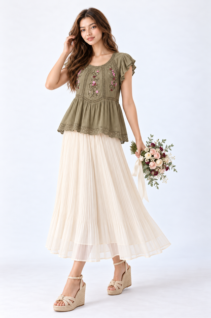 Model wearing an olive green floral embroidered peplum blouse with flutter sleeves and round neckline, styled with a cream pleated maxi skirt and wedge sandals.