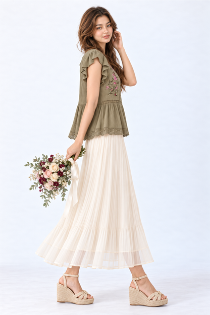 Model wearing an olive green floral embroidered peplum blouse with flutter sleeves and round neckline, styled with a cream pleated maxi skirt and wedge sandals.